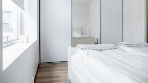 Ein modernes Schlafzimmer mit einem großen Spiegel, einem ordentlich bezogenen Bett und einem Fenster mit Blick ins Freie.