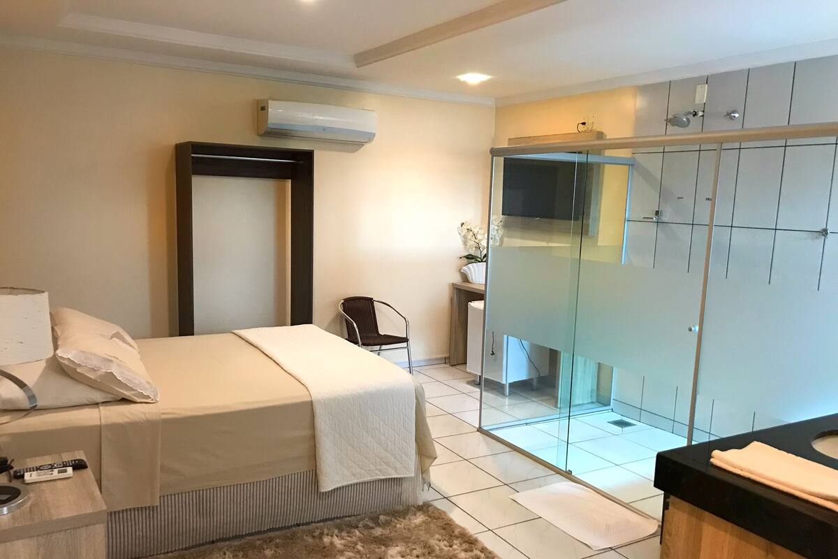 A modern bedroom with a bed, bedside table, and a glass-enclosed shower area.