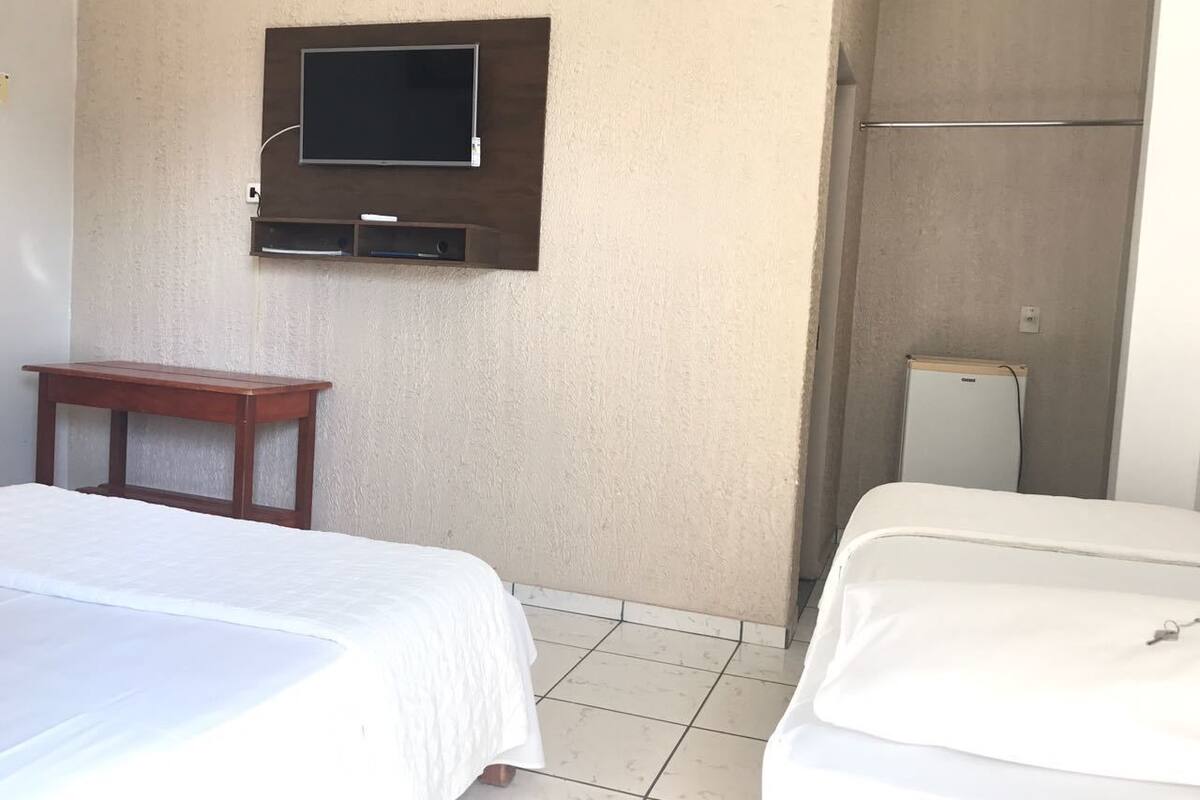 A hotel room with two beds, a TV mounted on the wall, a small wooden table, and a refrigerator.