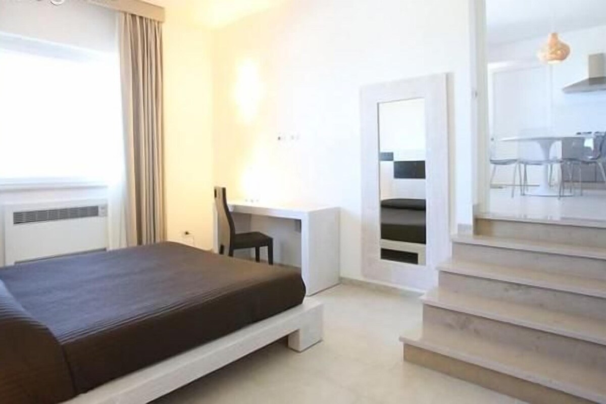 A hotel room with a bed, a desk, and a staircase.