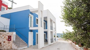 Un edificio moderno de dos pisos con fachada azul y blanca, una escalera de piedra y vista al mar.