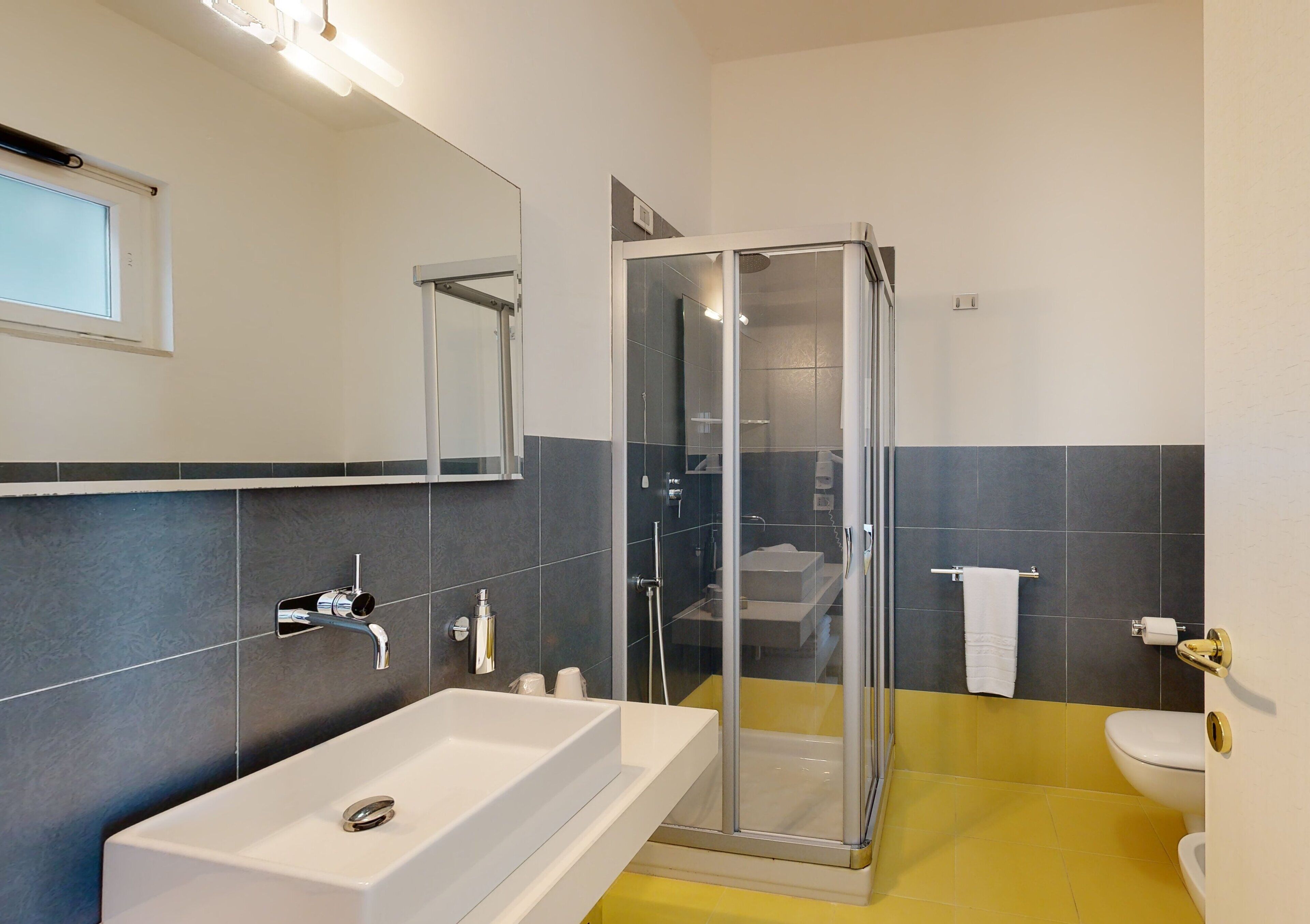 Une salle de bain moderne avec une douche en verre, un lavabo blanc et un sol carrelé de carreaux jaunes.