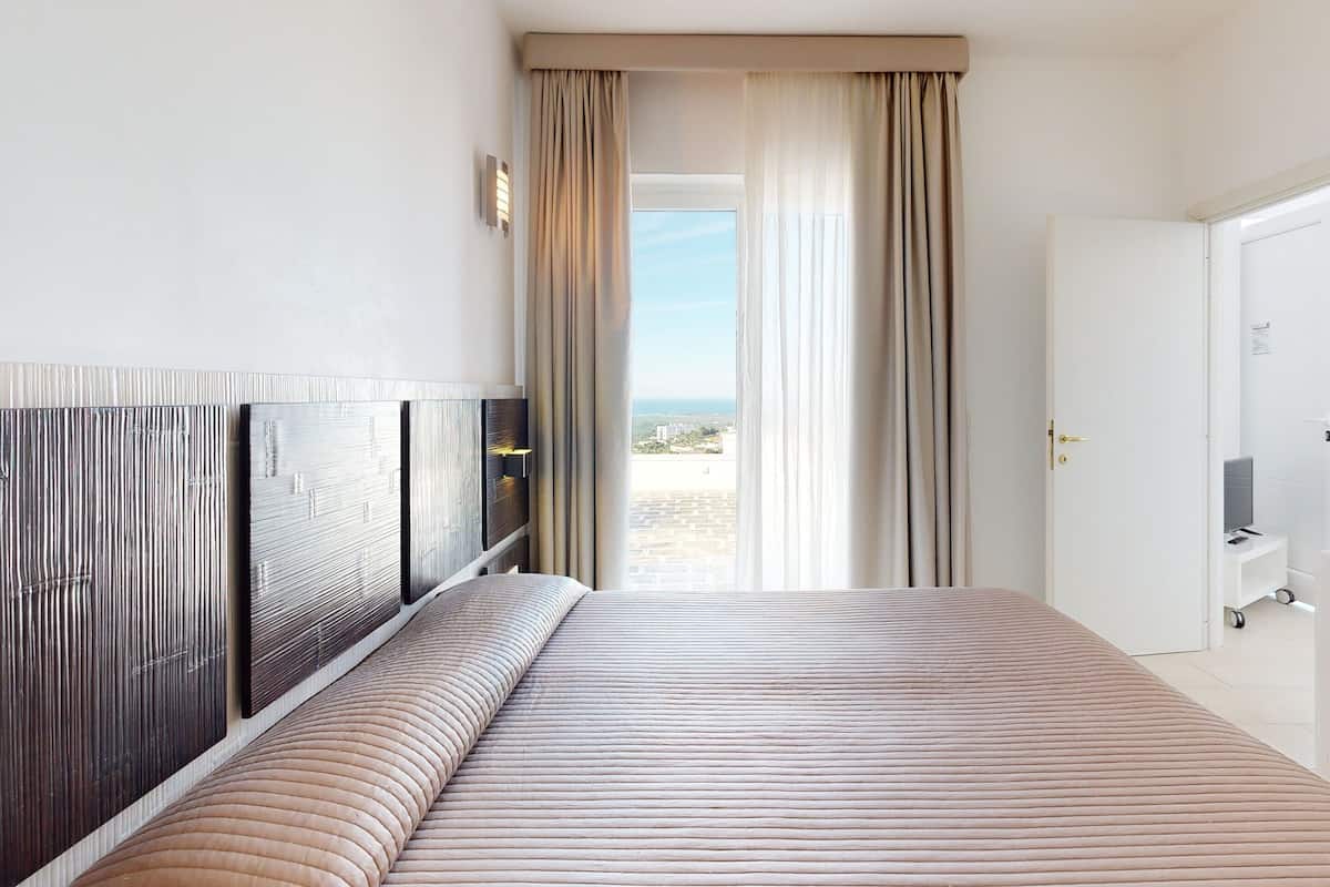 A hotel room with a large bed, a desk with a computer, and a view of the city through the window.