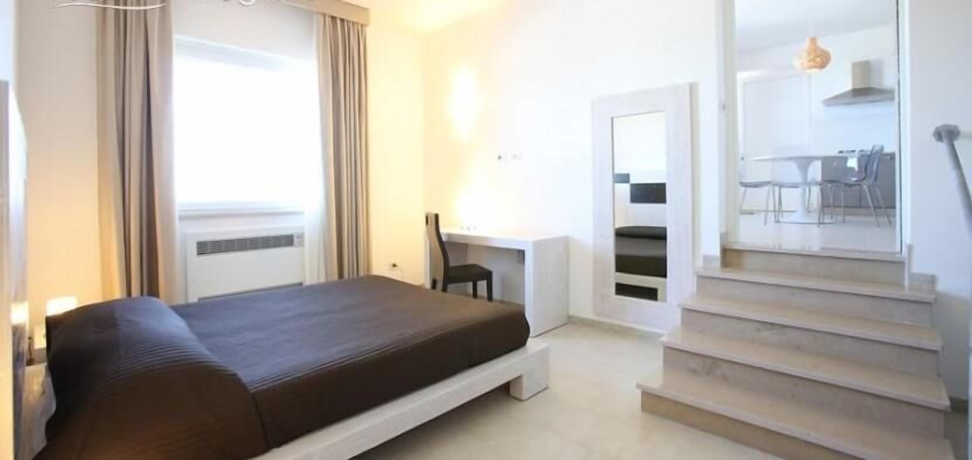 Une chambre à coucher comprenant un lit, un bureau et un escalier menant à une salle à manger.