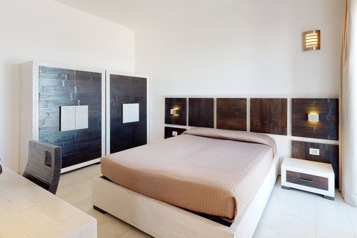 A modern bedroom with a large bed, built-in wardrobes, and bedside lamps.