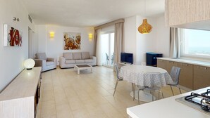 Una sala moderna con sofá, una mesa de centro y un comedor con mesa y sillas. Hay un televisor, una lámpara y una ventana con cortinas.