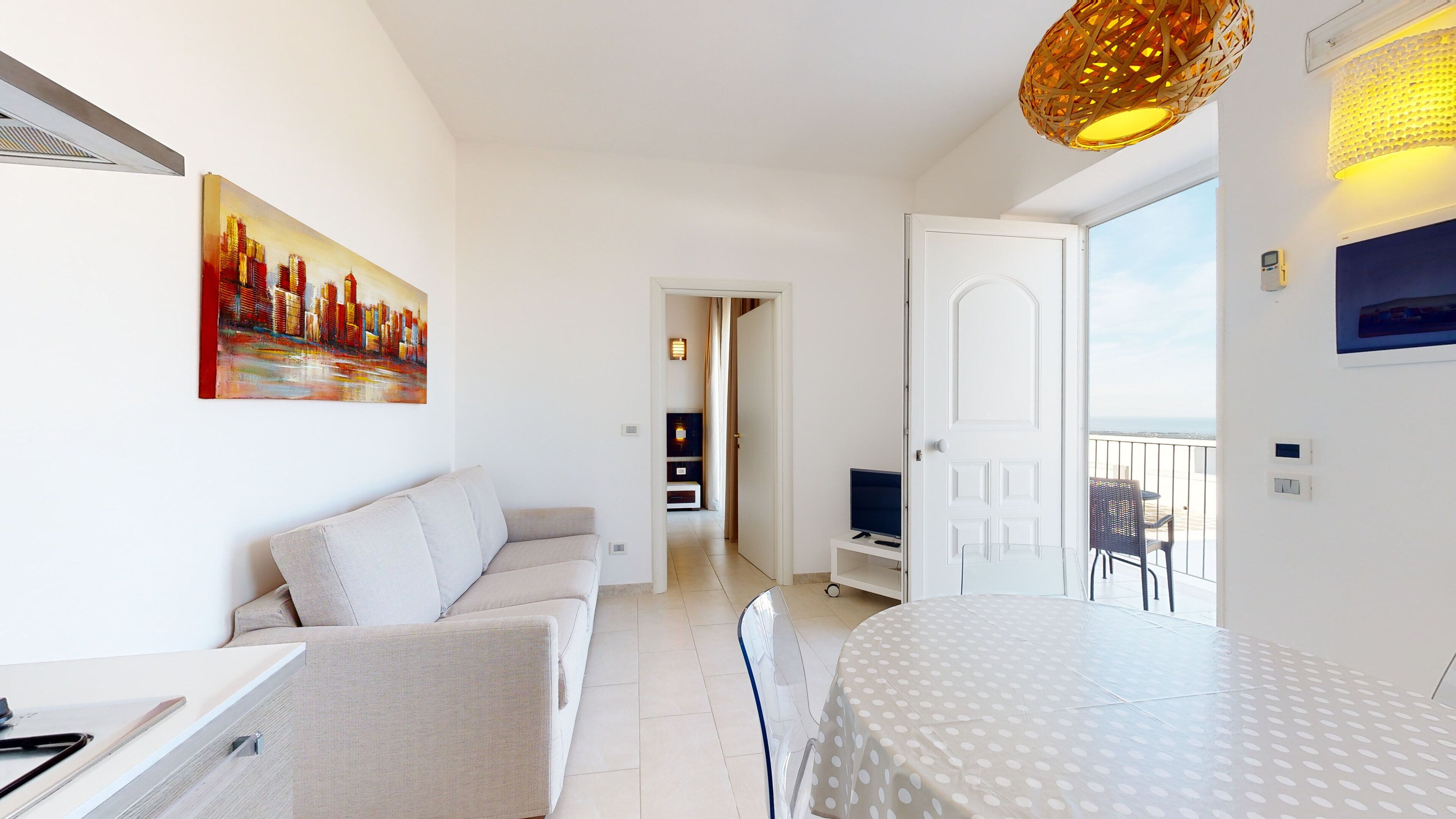 A modern hotel room with a sofa, a dining table, a TV, and a balcony with a view.