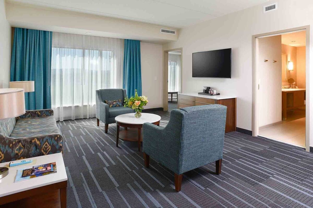 Habitación de hotel con sofá, sillón, mesita y televisor.