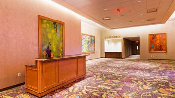 A hotel lobby with a reception desk, colorful artwork on the walls, and a patterned carpet.