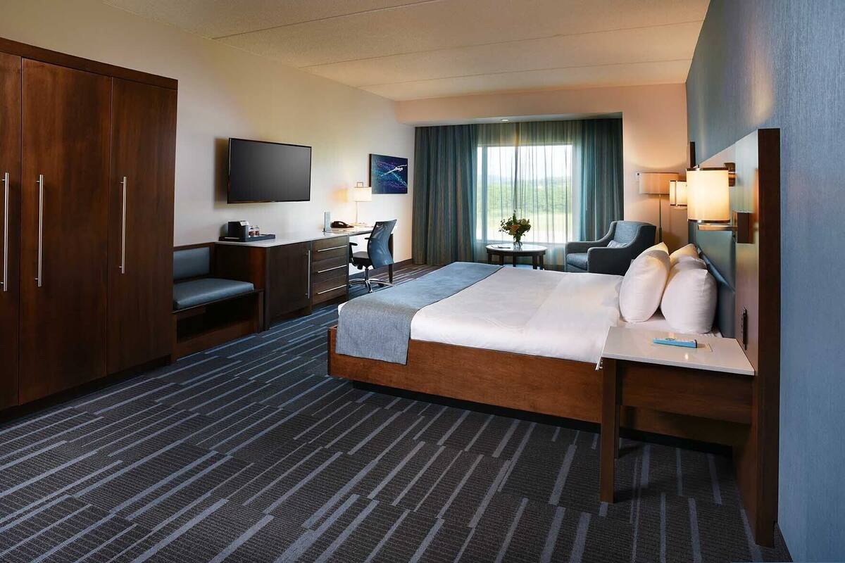 Habitación de hotel con una cama grande, un escritorio, una silla, un televisor y vistas al exterior.