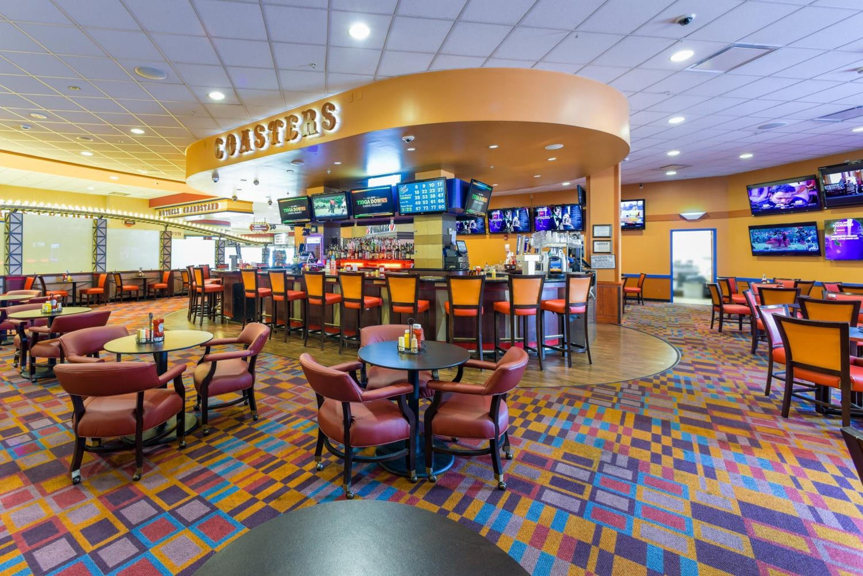 A restaurant with multiple seating areas, including round tables and booths, and a bar area with multiple screens.