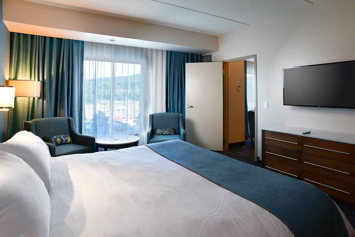 Habitación de hotel con una cama grande, dos sillones, una mesita, un televisor y vistas al exterior.
