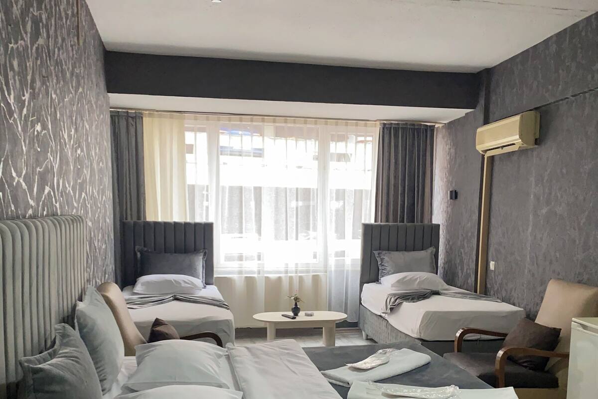 Una habitación de hotel con dos camas, una mesita pequeña, una silla y una mesita de noche con lámpara.