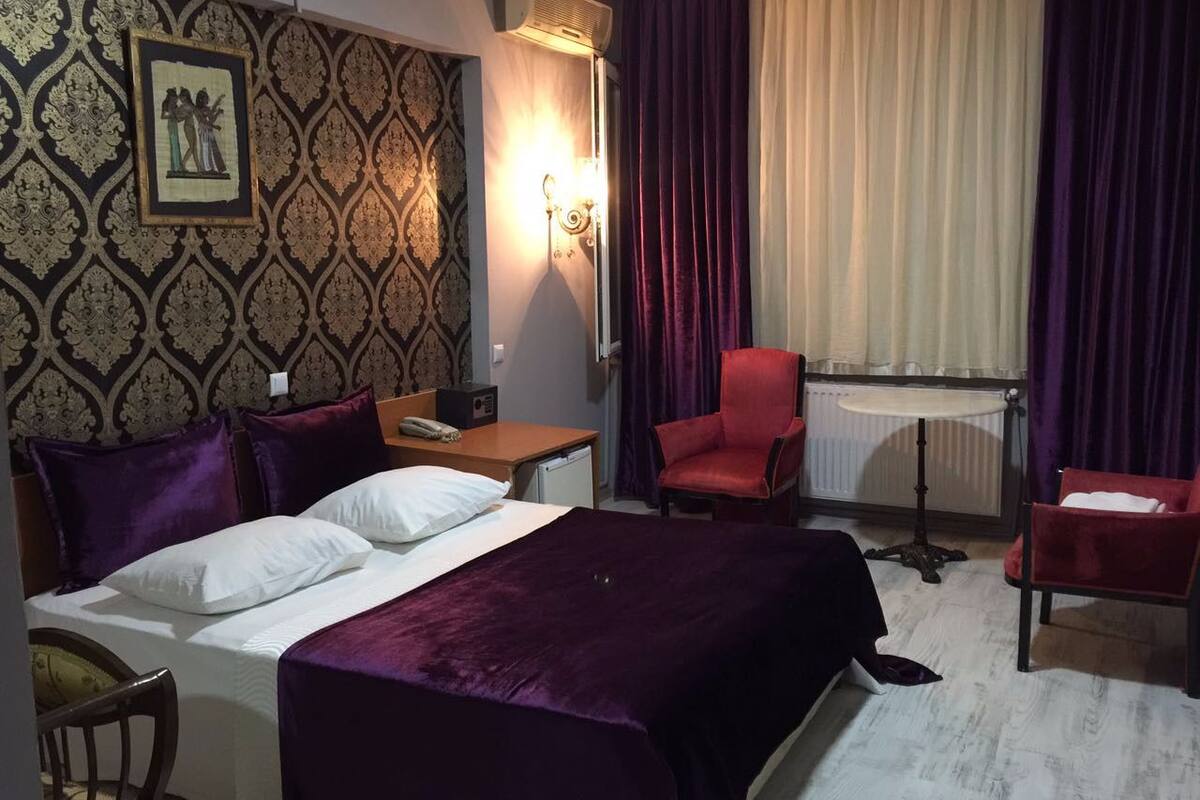 Habitación de hotel con una cama grande, dos sillas, una mesita y un aire acondicionado instalado en la pared.