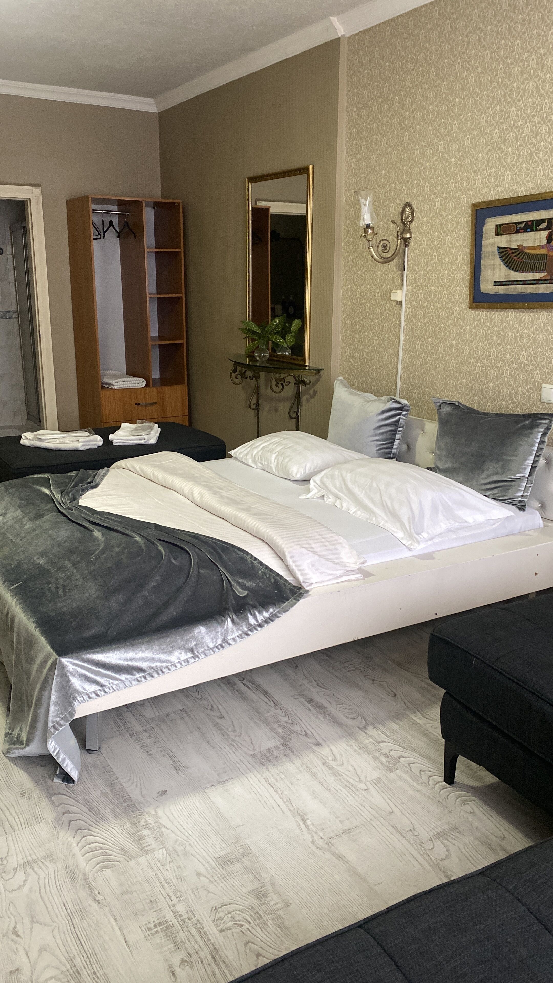A bedroom with a bed, bedside tables, a wardrobe, a mirror, a lamp, and a wall-mounted artwork.