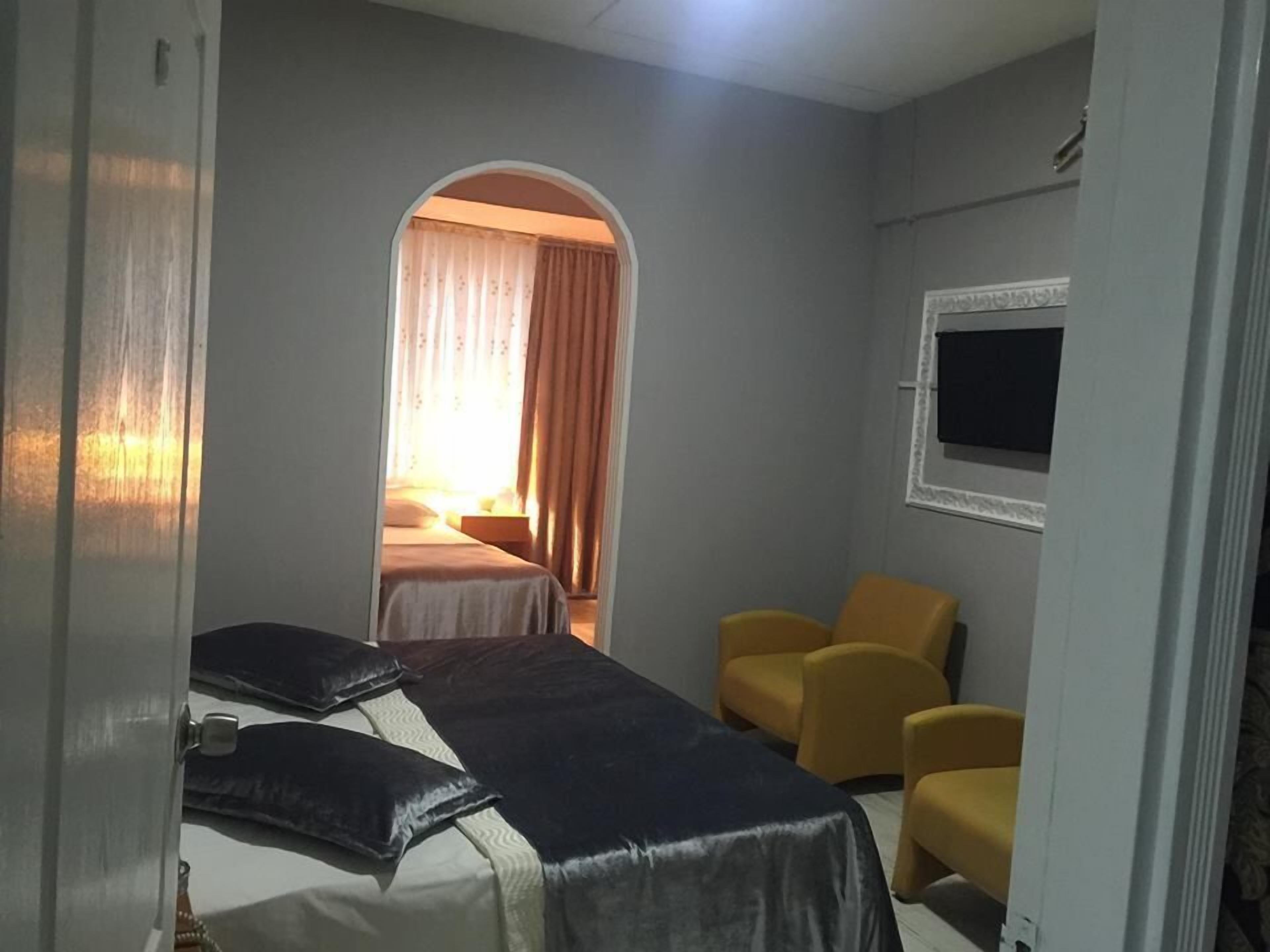 A hotel room with a bed, two yellow chairs, a TV, and a window with curtains.