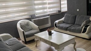 A modern living room with a sofa, armchair, and coffee table, featuring a radiator and a window with blinds. - Masal Otel (Izmit)