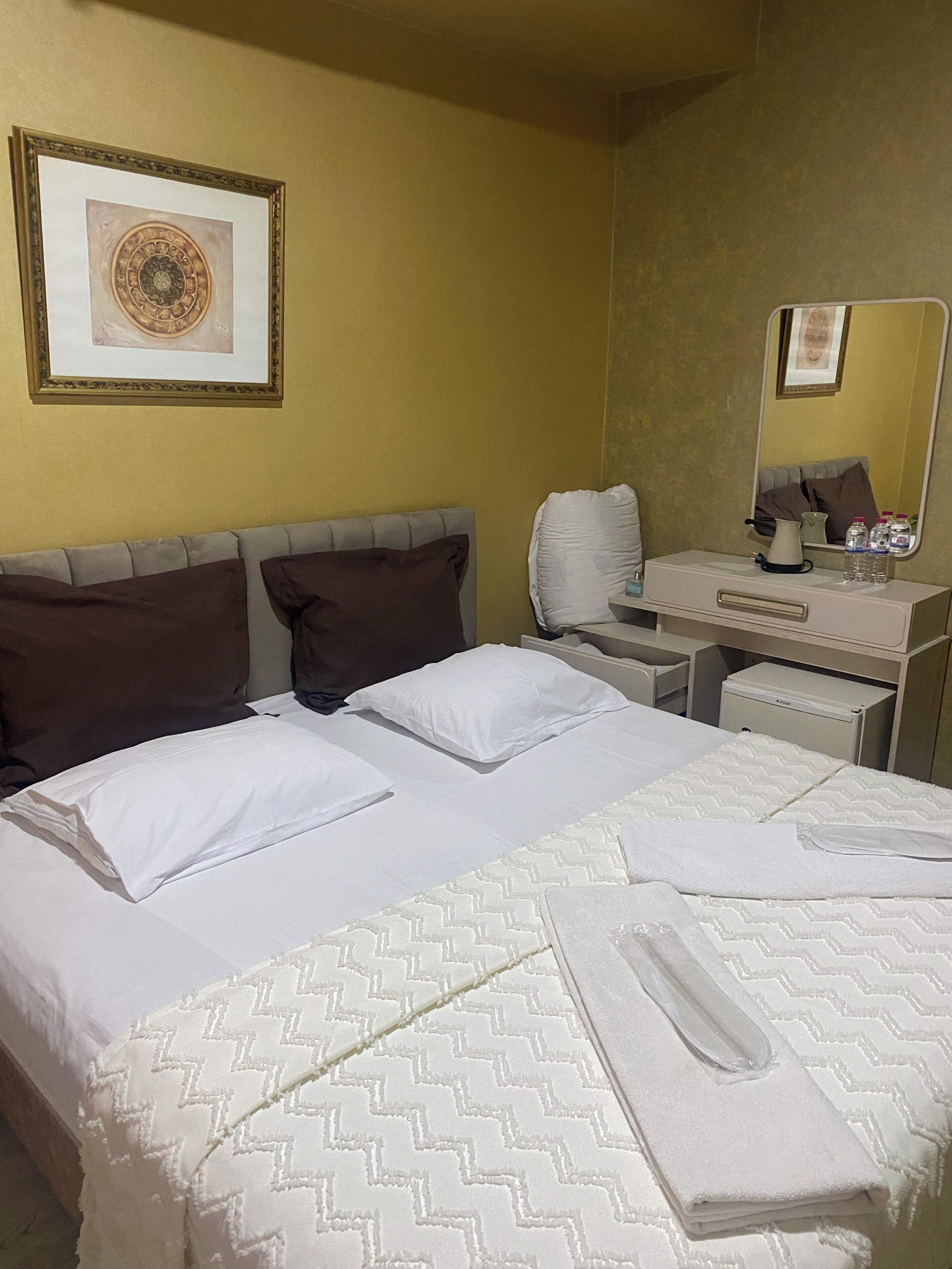 A hotel room with a bed, a desk, a chair, a mirror, and a framed picture on the wall.