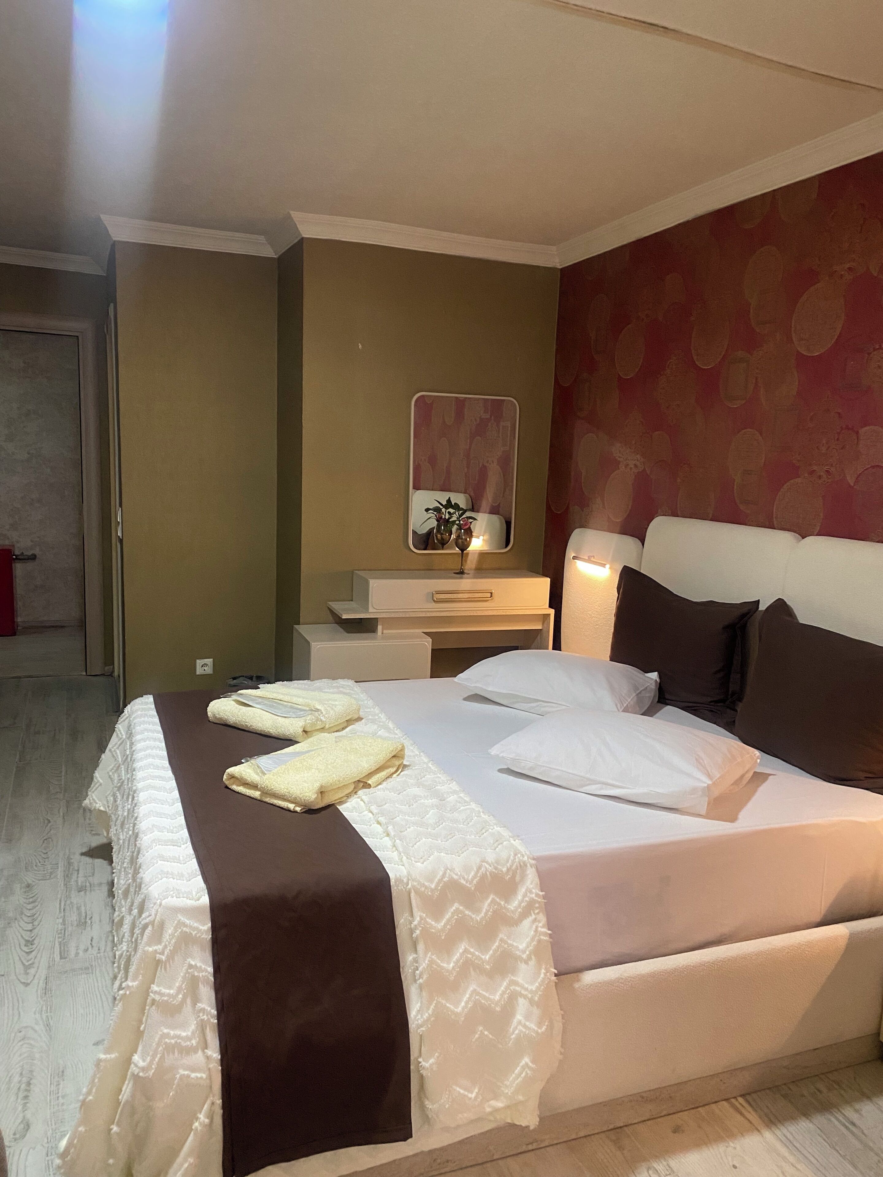 Un lit bien fait, avec une tête de lit marron, une table de chevet avec une lampe et un miroir accroché au mur.