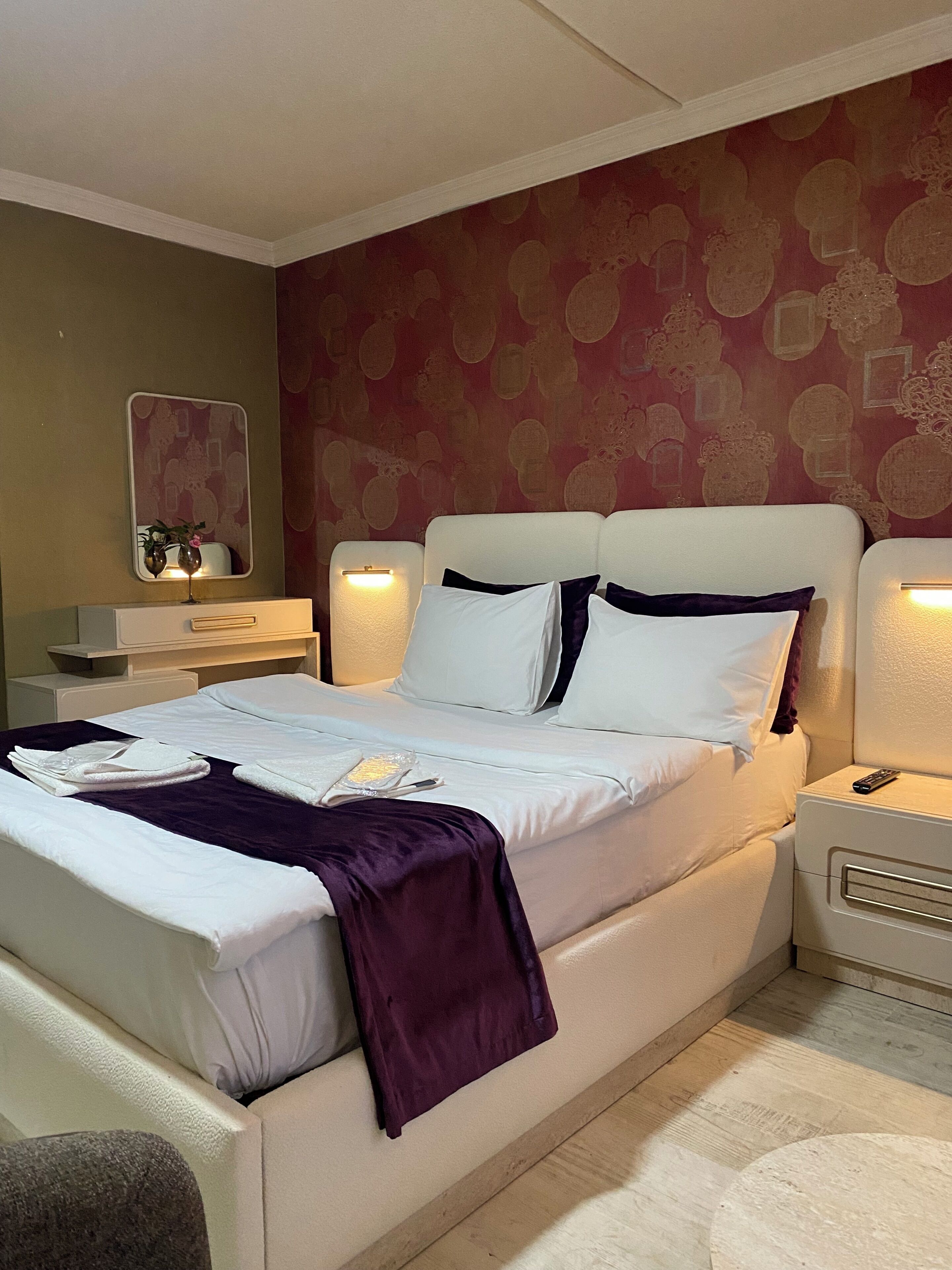 A hotel room with a large bed, bedside tables, a mirror, and a patterned wall.