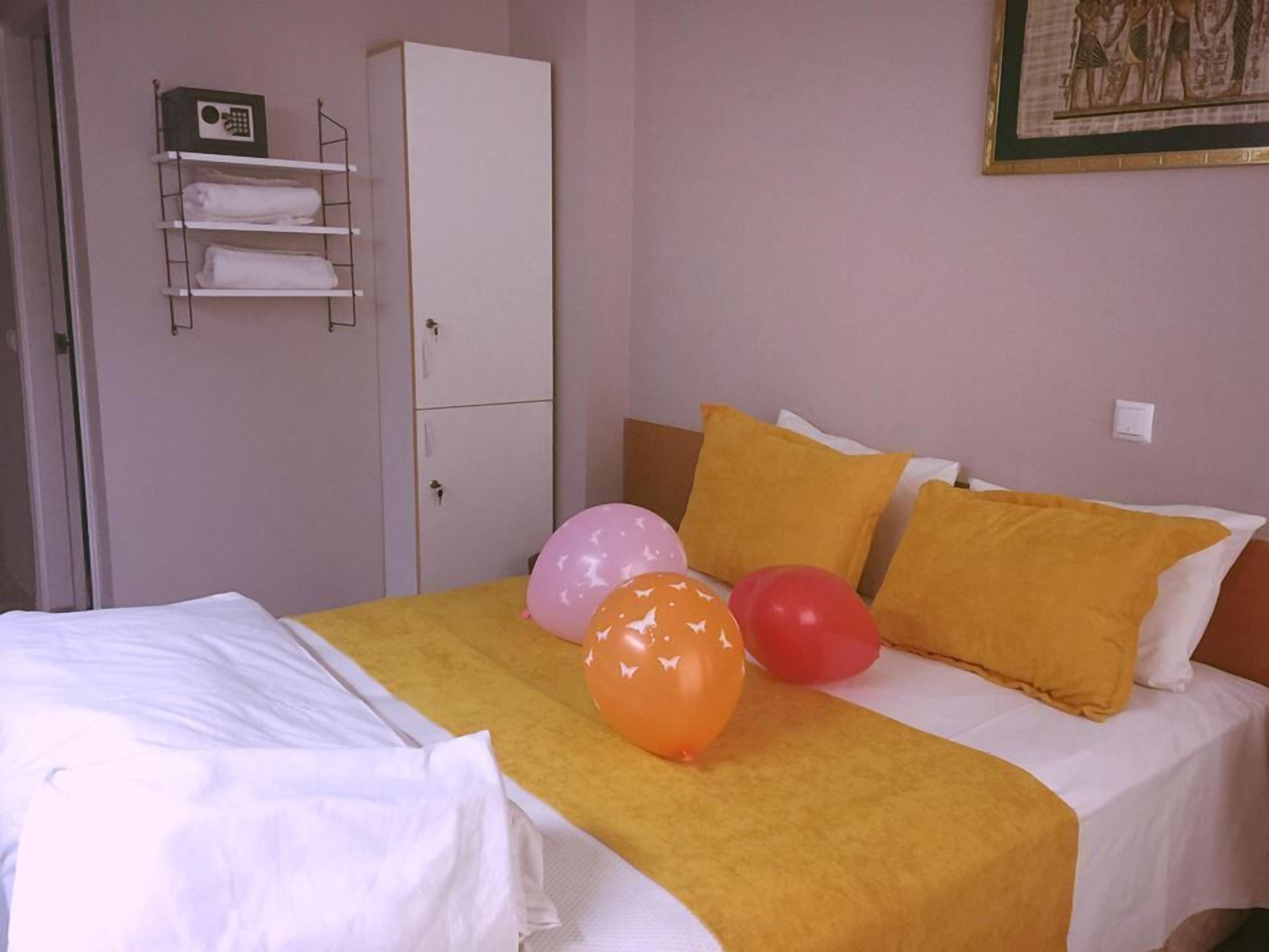 Una habitación de hotel con una cama, almohadas amarillas y globos.