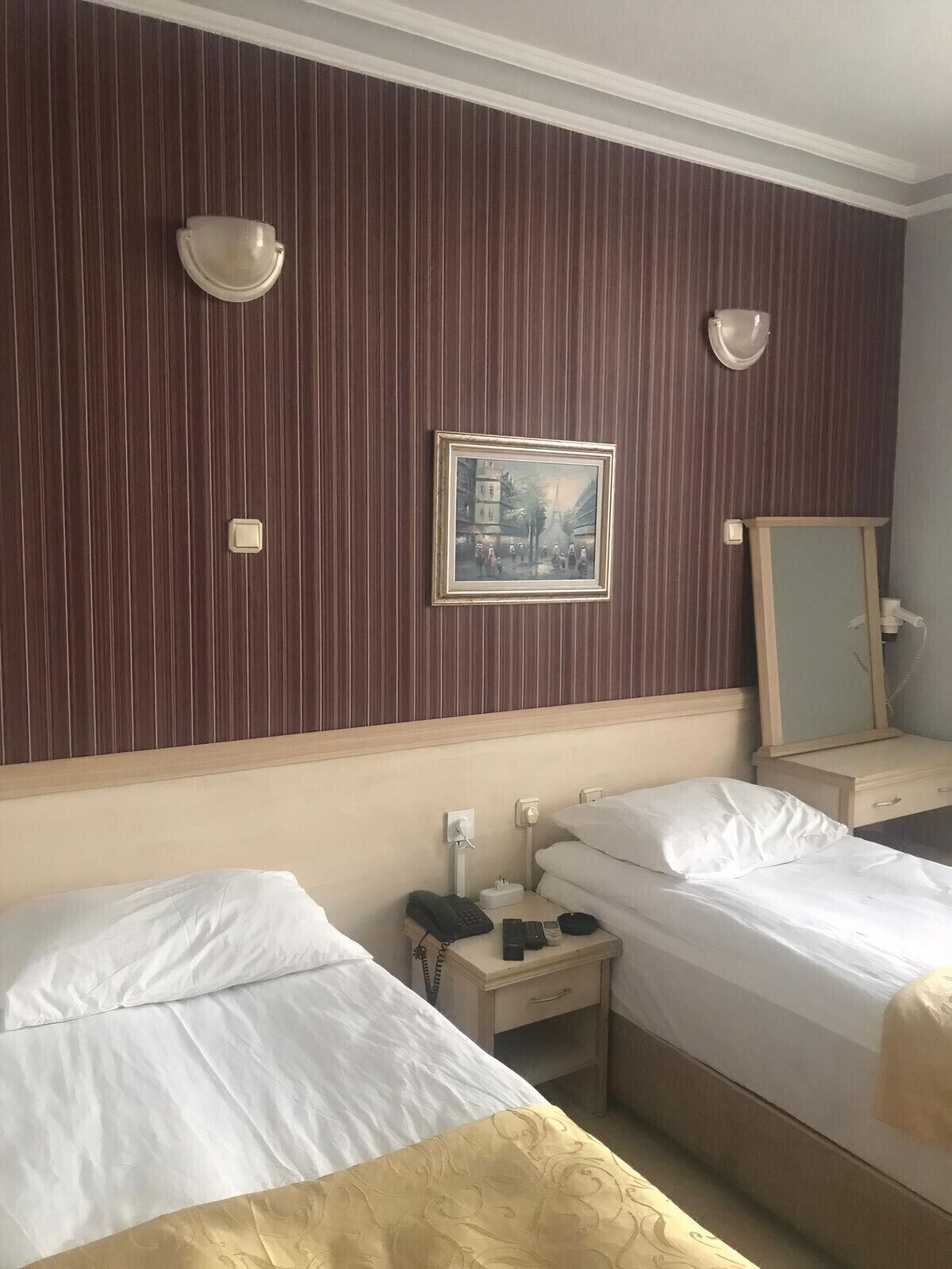 A hotel room with two beds, a bedside table with a phone, a mirror, and a framed picture on the wall.