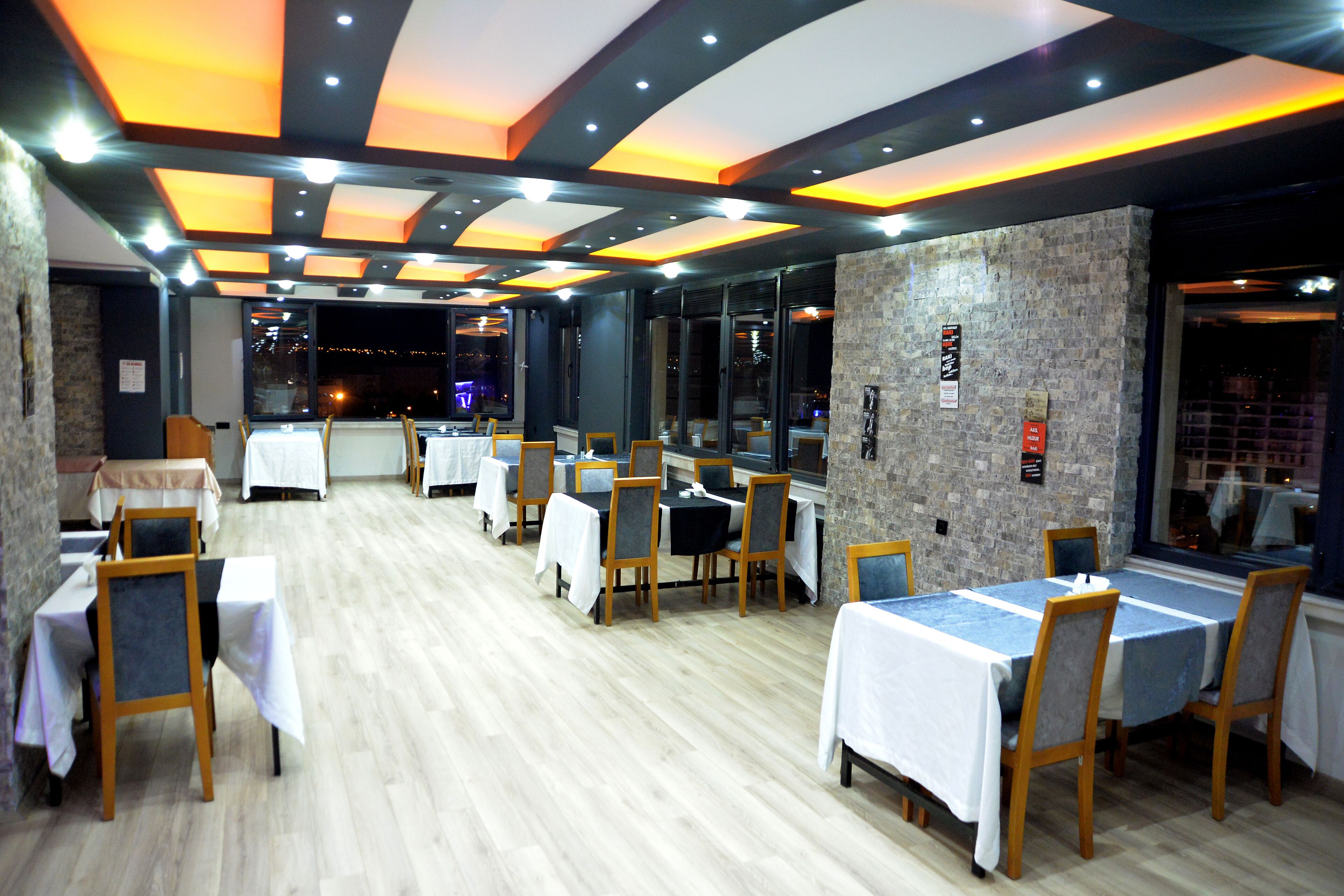 Un restaurante con varias mesas y sillas, suelo de madera y un diseño de techo moderno.