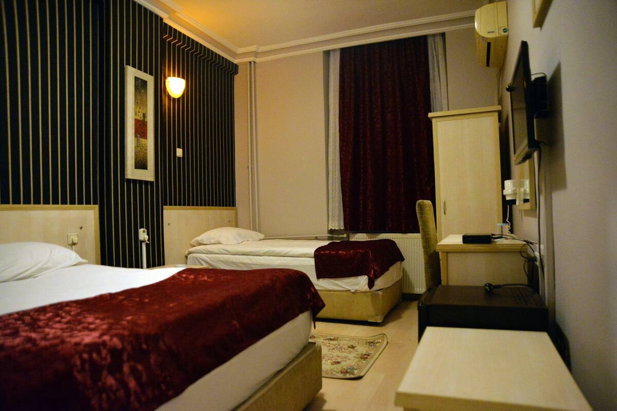 Ein Hotelzimmer mit zwei Betten, einem Schreibtisch, einem Stuhl, einem Fernseher und einem Vorhangfenster.