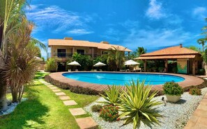 Una piscina rodeada por un jardín con palmeras y un edificio con techo de tejas.