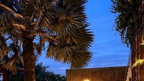 Un espace extérieur bien éclairé, agrémenté d’un mur en pierre, d’une clôture en bois et d’un chemin menant à un bâtiment dont la façade est ornée d’un motif en forme de croissant de lune.