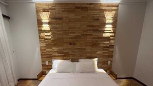 Une chambre d’hôtel avec une tête de lit en bois, un lit bien fait avec du linge de maison blanc et deux lampes fixées au mur.