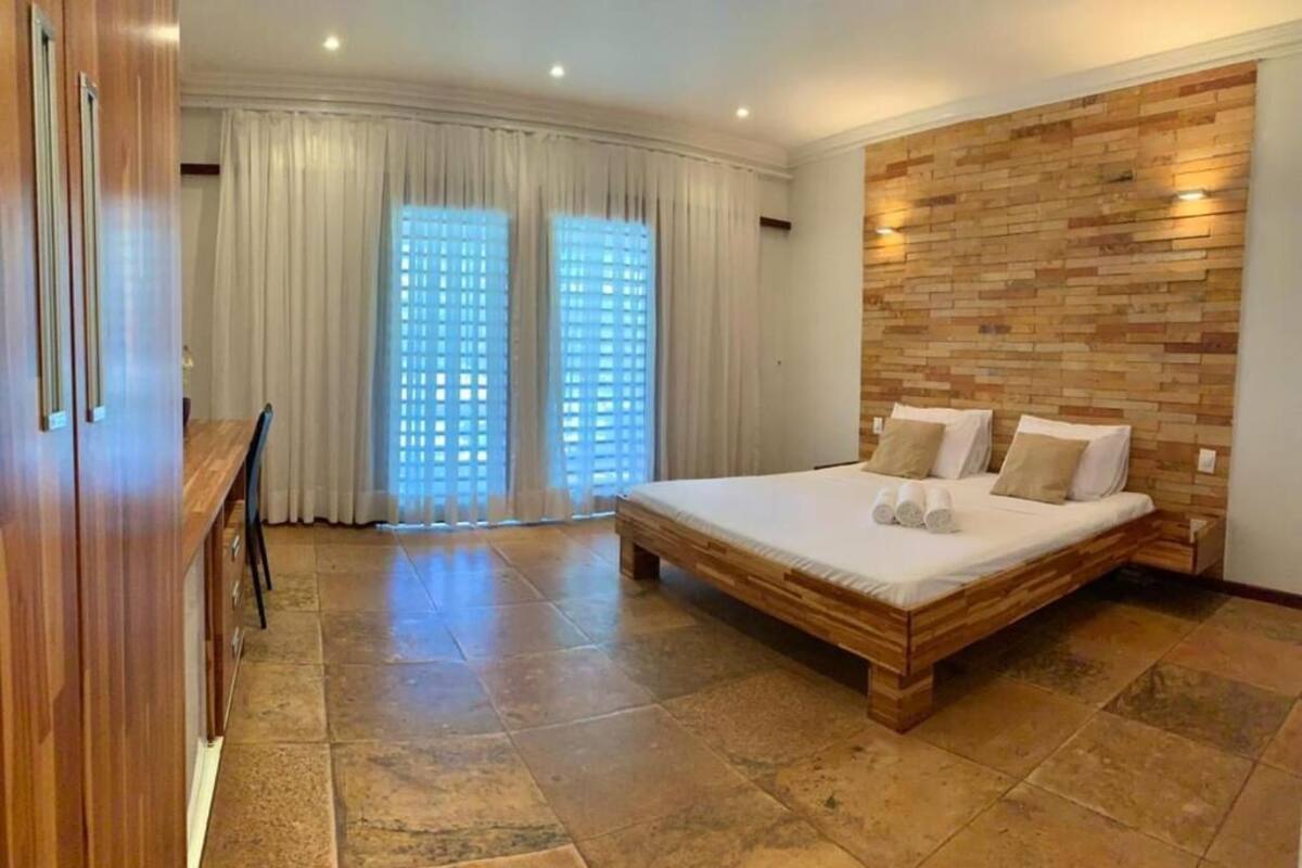 A bedroom with a large bed, wooden headboard, and a view through a window with curtains.