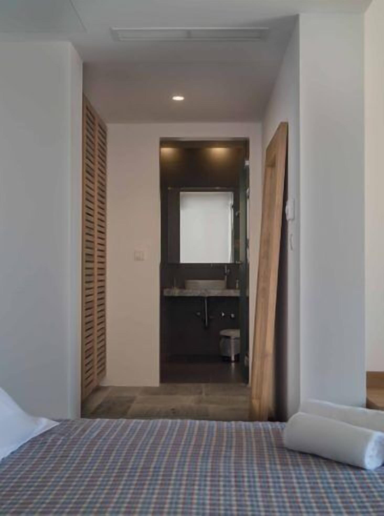 Un dormitorio con cama, una puerta de madera y vistas a un baño con lavabo e inodoro.