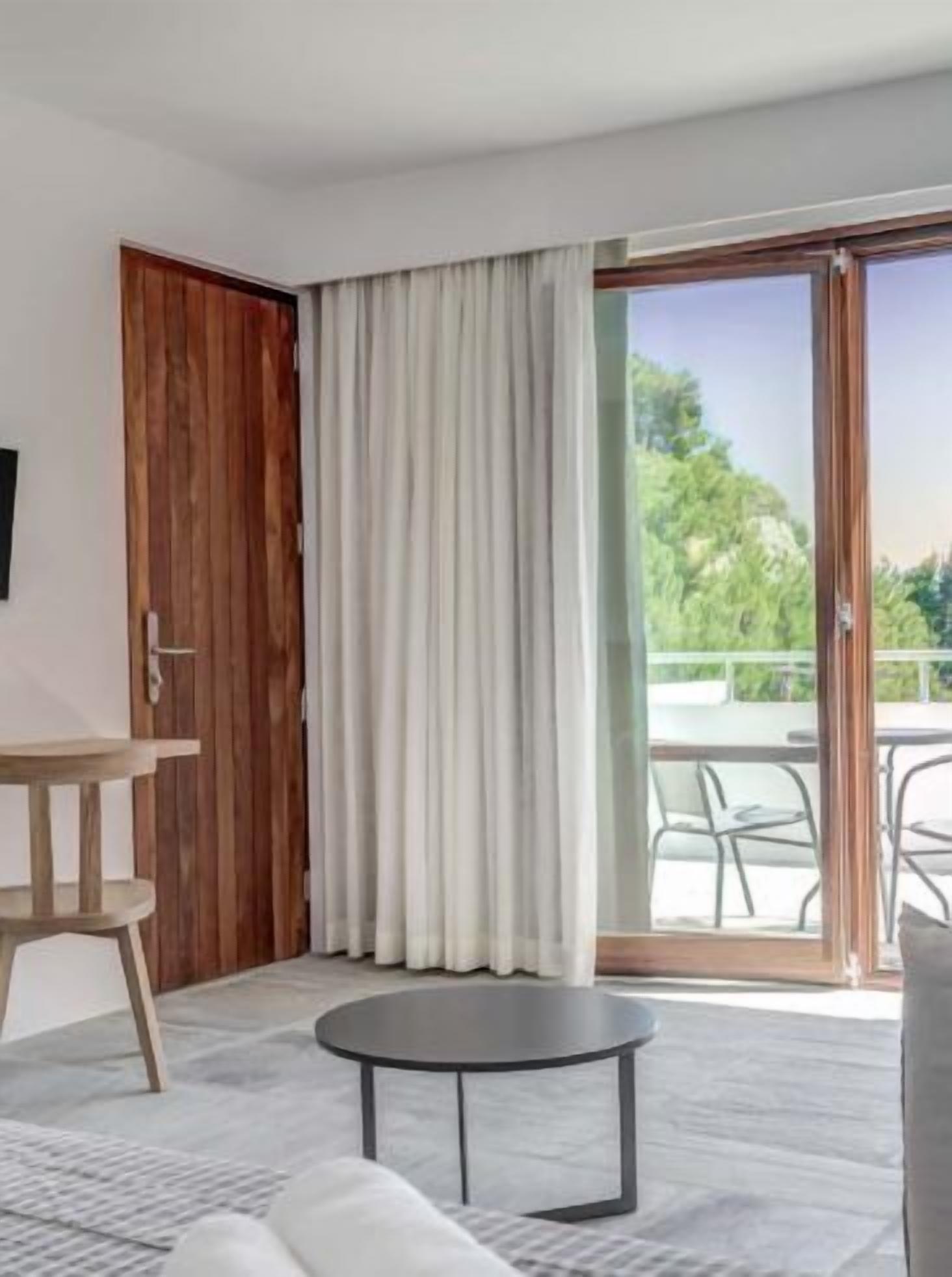 Ein modernes Zimmer mit einem runden schwarzen Tisch, einer Couch, einer Holztür und einem großen Schiebeglasfenster, das zu einem Außenbereich mit Stühlen führt.
