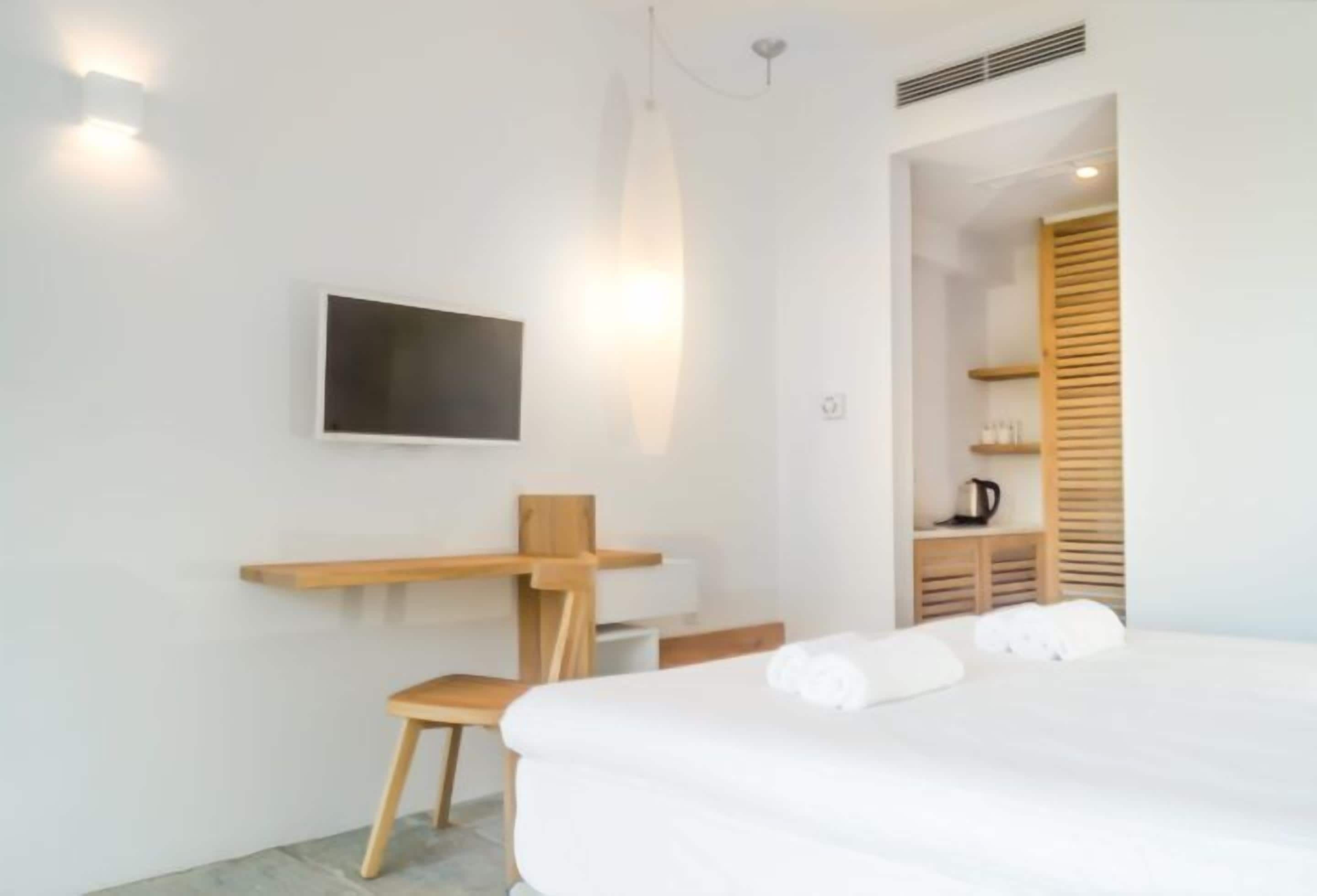 Une chambre d’hôtel moderne équipée d’un lit, d’un bureau, d’une chaise, d’un téléviseur fixé au mur et d’une armoire en bois.