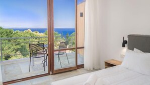 Ein Schlafzimmer mit einer großen Schiebeglasdoor, die auf einen Balkon mit Blick auf das Meer und die grüne Umgebung führt.