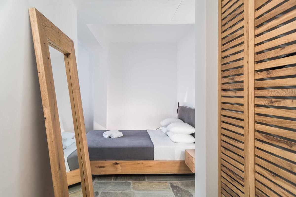 A small, neatly arranged bedroom with a single bed, a wooden headboard, and a stone floor.