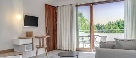 Una habitación moderna con sofá, una mesita, televisor en la pared y balcón con mobiliario exterior.
