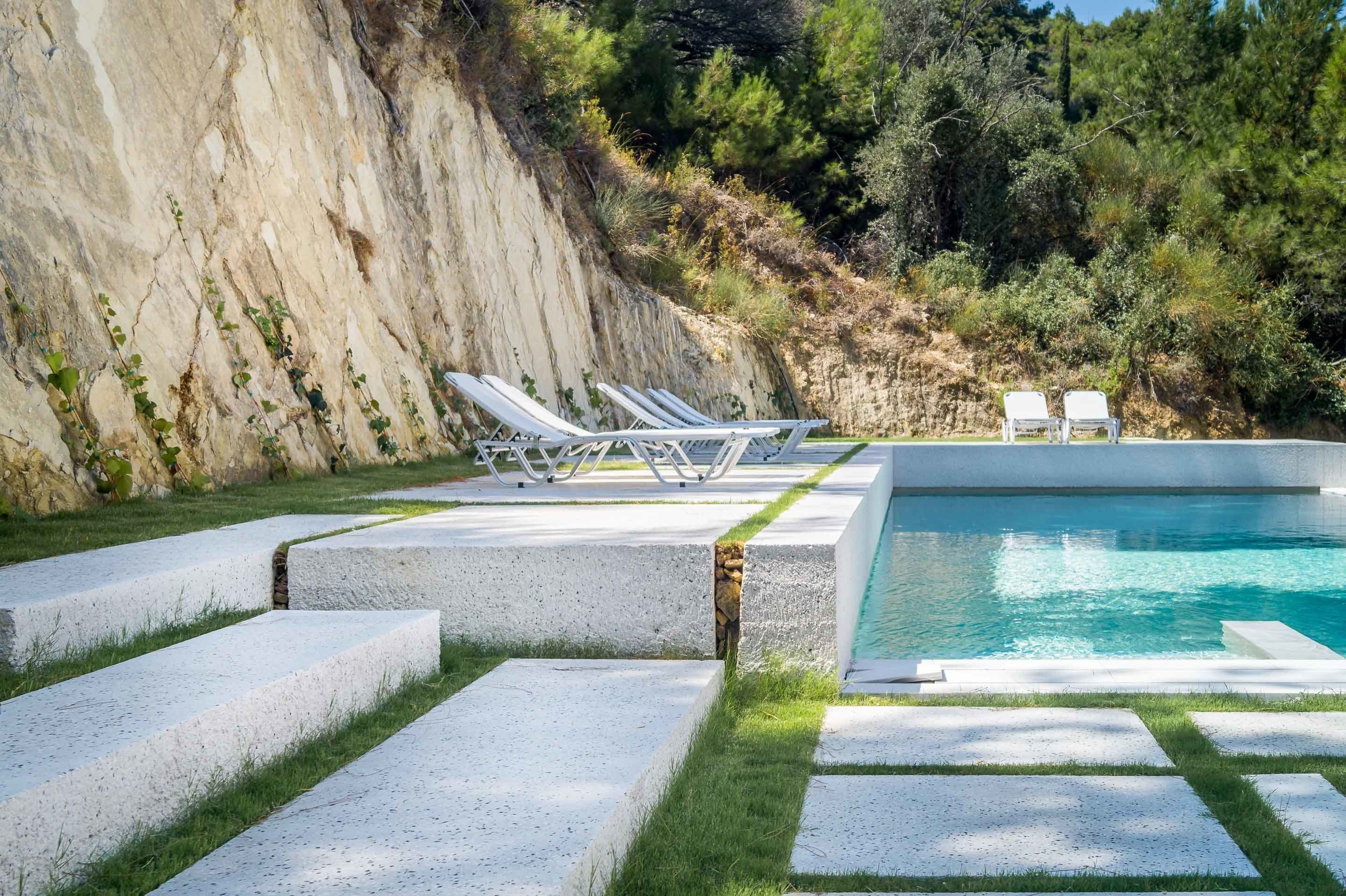 A swimming pool with white lounge chairs and a stone wall.