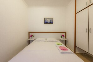 A small, neatly arranged bedroom with a single bed, two bedside tables with flower vases, a framed picture on the wall, and a wardrobe.