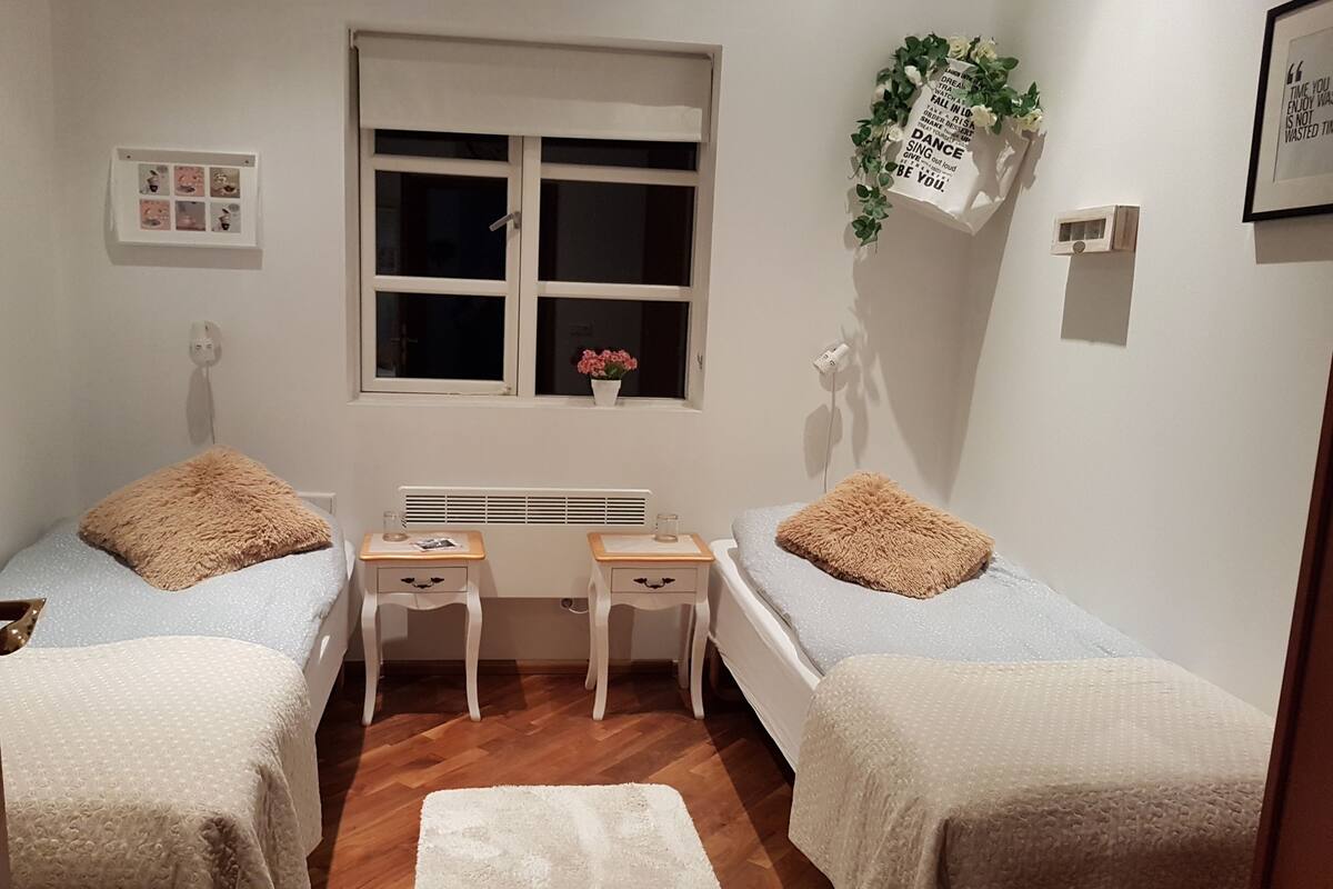 A small, tidy room with two single beds, a small table, a window, and a radiator.