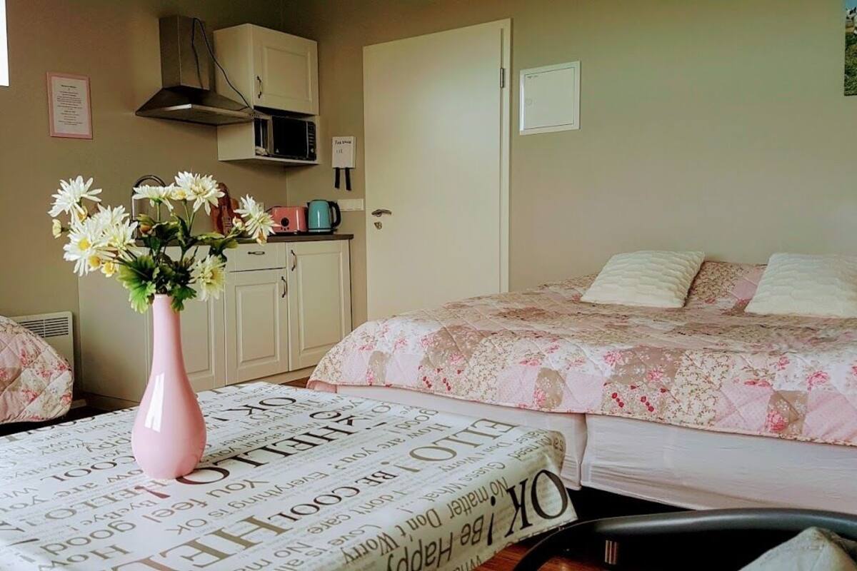 A bedroom with two beds, a pink vase with flowers, a microwave, and a door with a sign.