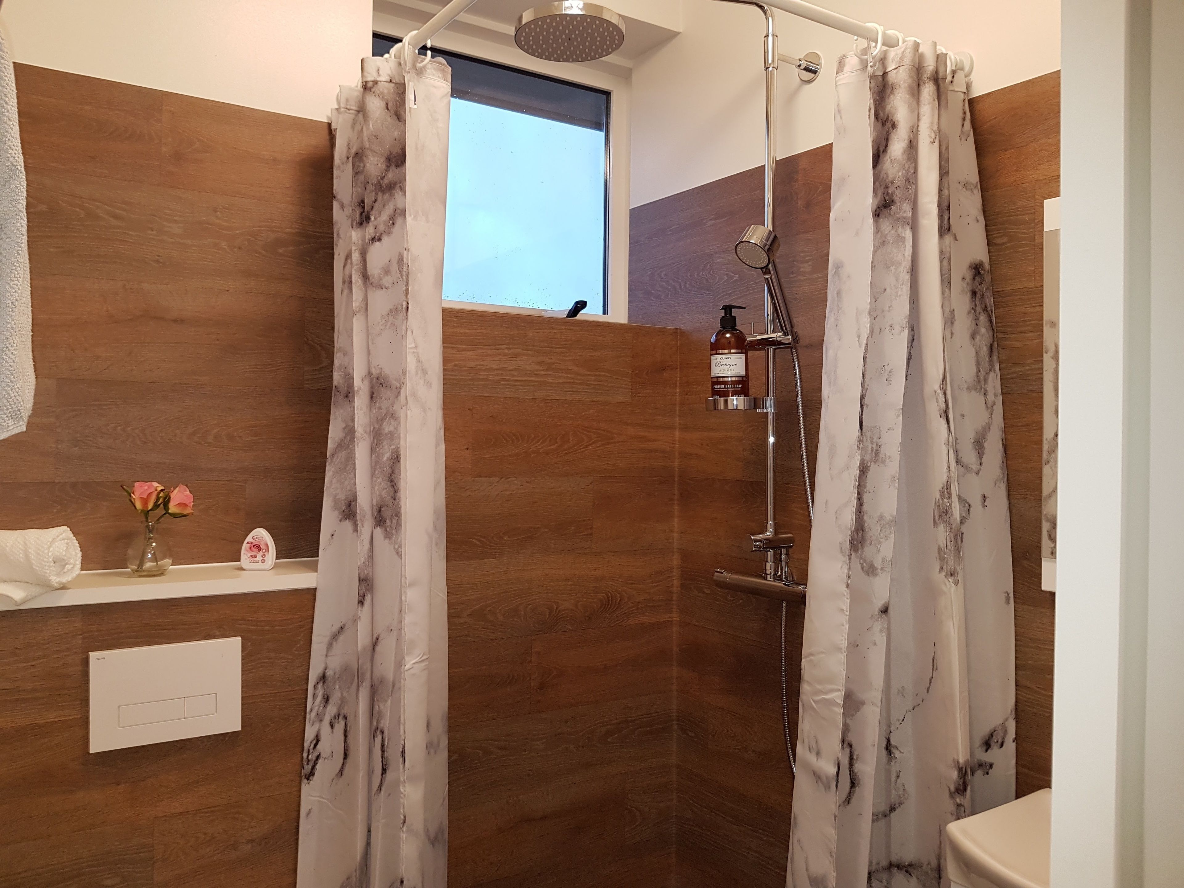 A modern bathroom with a shower, a vanity with a soap dispenser, and a window.