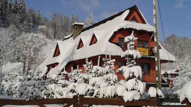 A snow-covered building with a red roof and multiple windows, surrounded by snow-laden trees and a clear sky. - Willa Pod Bandera (Zakopane)