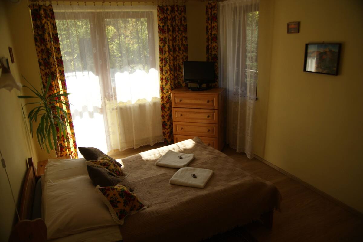 A bedroom with a bed, a dresser, a television on top, and a window with curtains.