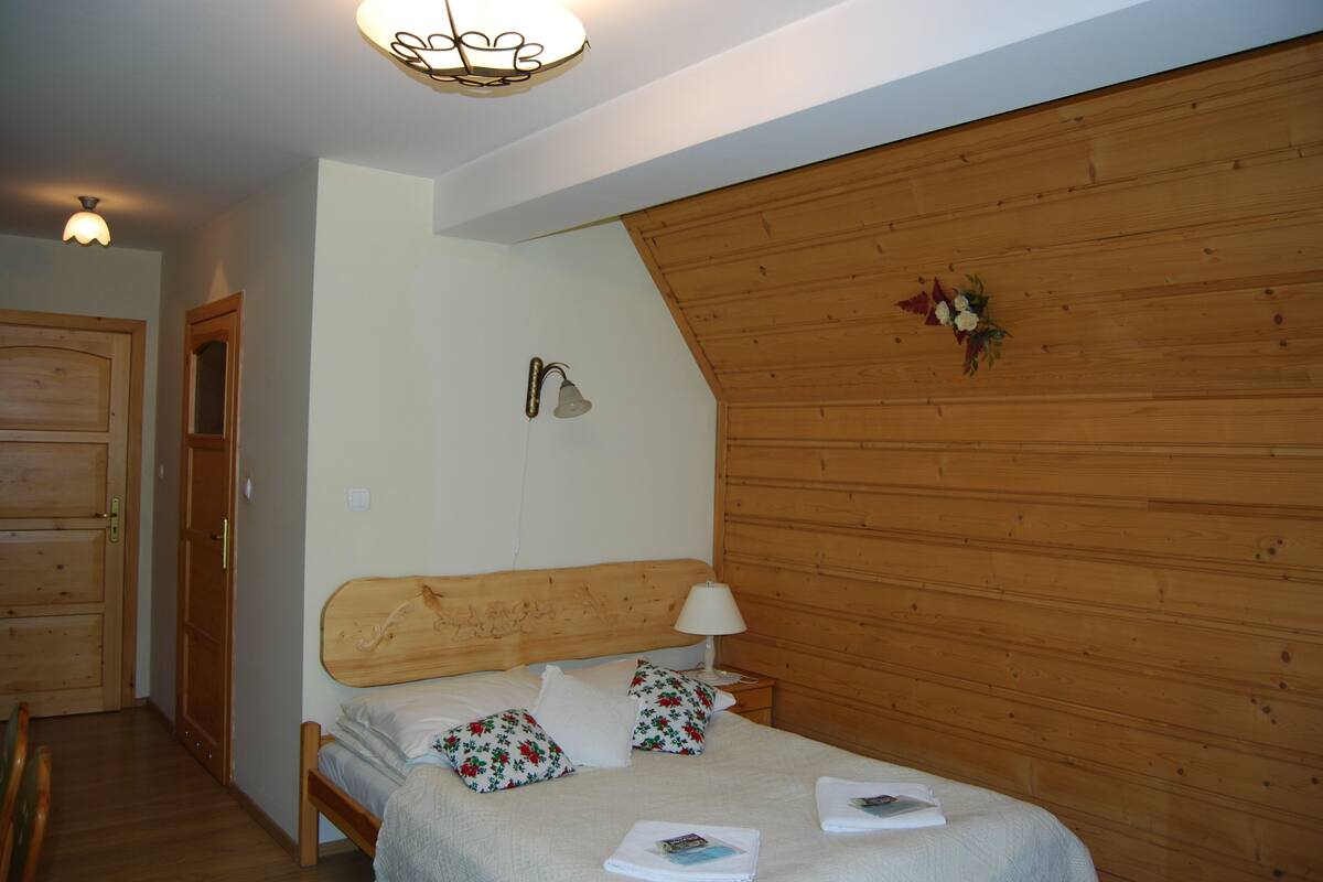 A bedroom with a wooden headboard, a bedside table with a lamp, and floral-patterned pillows.