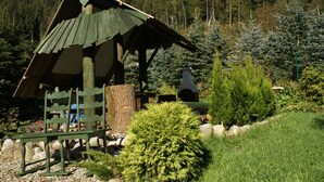 A rustic wooden structure with a sloped roof, surrounded by lush greenery and trees. - Willa Pod Bandera (Zakopane)