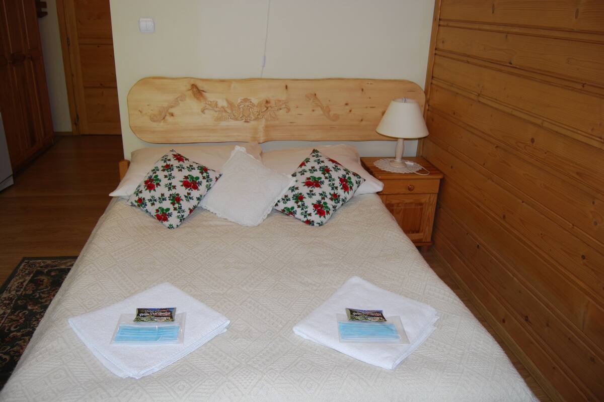 A neatly made bed with floral pillows, a wooden headboard, and a bedside table with a lamp.