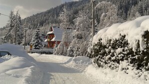 A snow-covered road with a building on the left and a forested hill in the background. - Willa Pod Bandera (Zakopane)