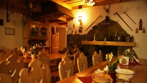 A rustic dining area with wooden tables and chairs, a stone fireplace, and various kitchen utensils displayed on the wall. - Willa Pod Bandera (Zakopane)